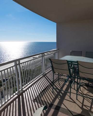 Oceanfront balcony with dining table, chairs, and metal railing overlooking calm blue sea