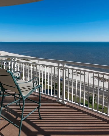 Oceanfront balcony with metal chair overlooking sandy beach and calm blue water
