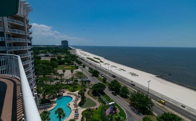 Beachfront high-rise resort with pool, landscaped grounds, sandy beach, and calm ocean under clear blue sky